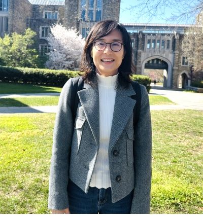 Woman with dark hair and glasses wearing a gray jacket. 